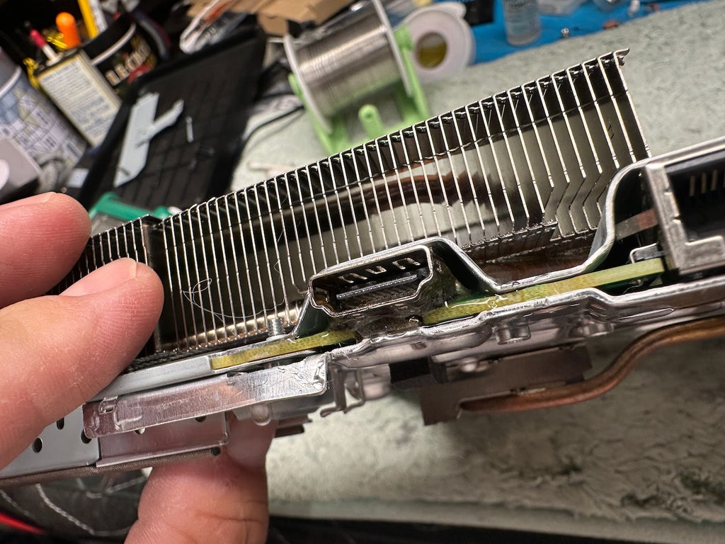 Close-up of a repaired PS5 HDMI port with cooling fins held by a hand, against a blurred background.